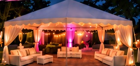 A 10 by 20 tent with white drapes, string lights and white lounge sofas